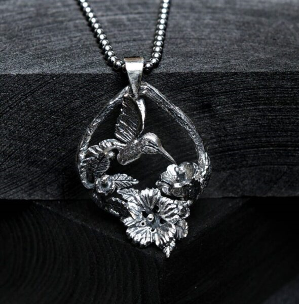 Pandantiv handmade din argint 925 cu pasăre colibri și flori hibiscus, fotografiat în decor de primăvară cu lavandă – bijuterie unicat inspirată din natură