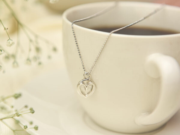 Pandantiv inimă din argint 925 așezat lângă o ceașcă de cafea – imagine romantică, perfectă pentru Valentine’s Day sau aniversări.